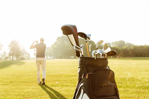 Man hitting golf ball with clubs in the background